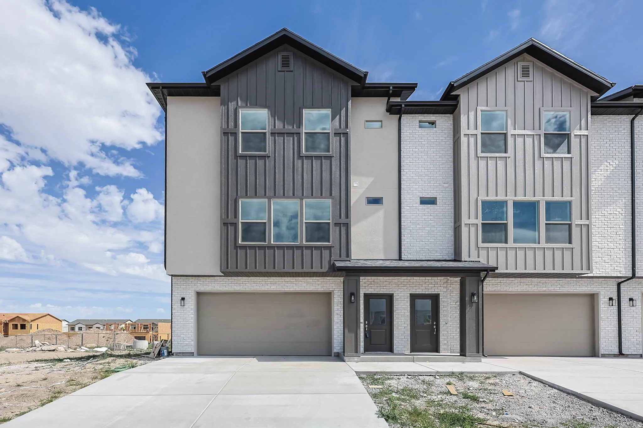 View of front of property with board and batten siding, an attached garage, concrete driveway, and a residential view. Middle unit