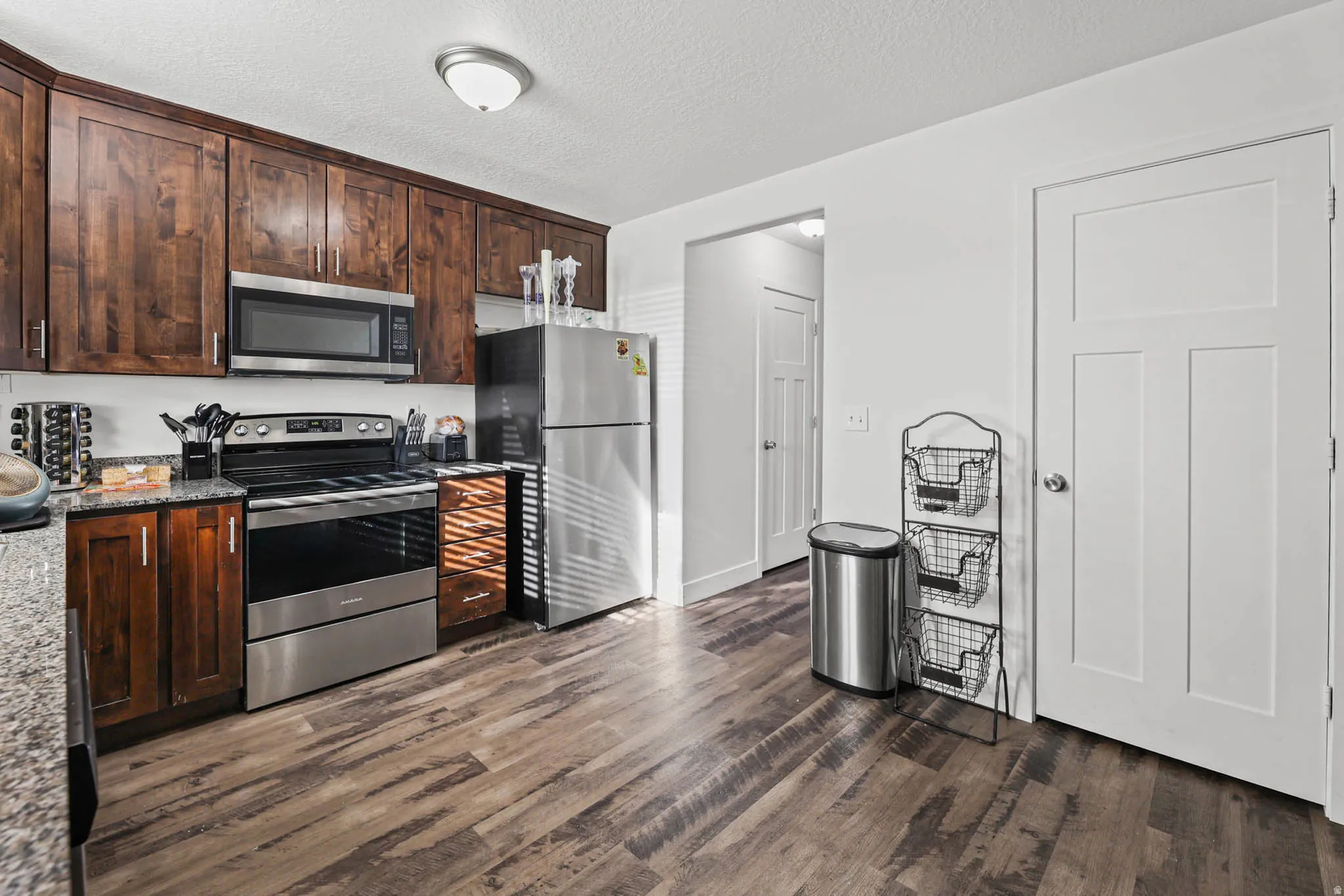 Kitchen featuring dark wood finish cabinets, stainless steel appliances, dark wood-style flooring, dark stone countertops, and a textured ceiling