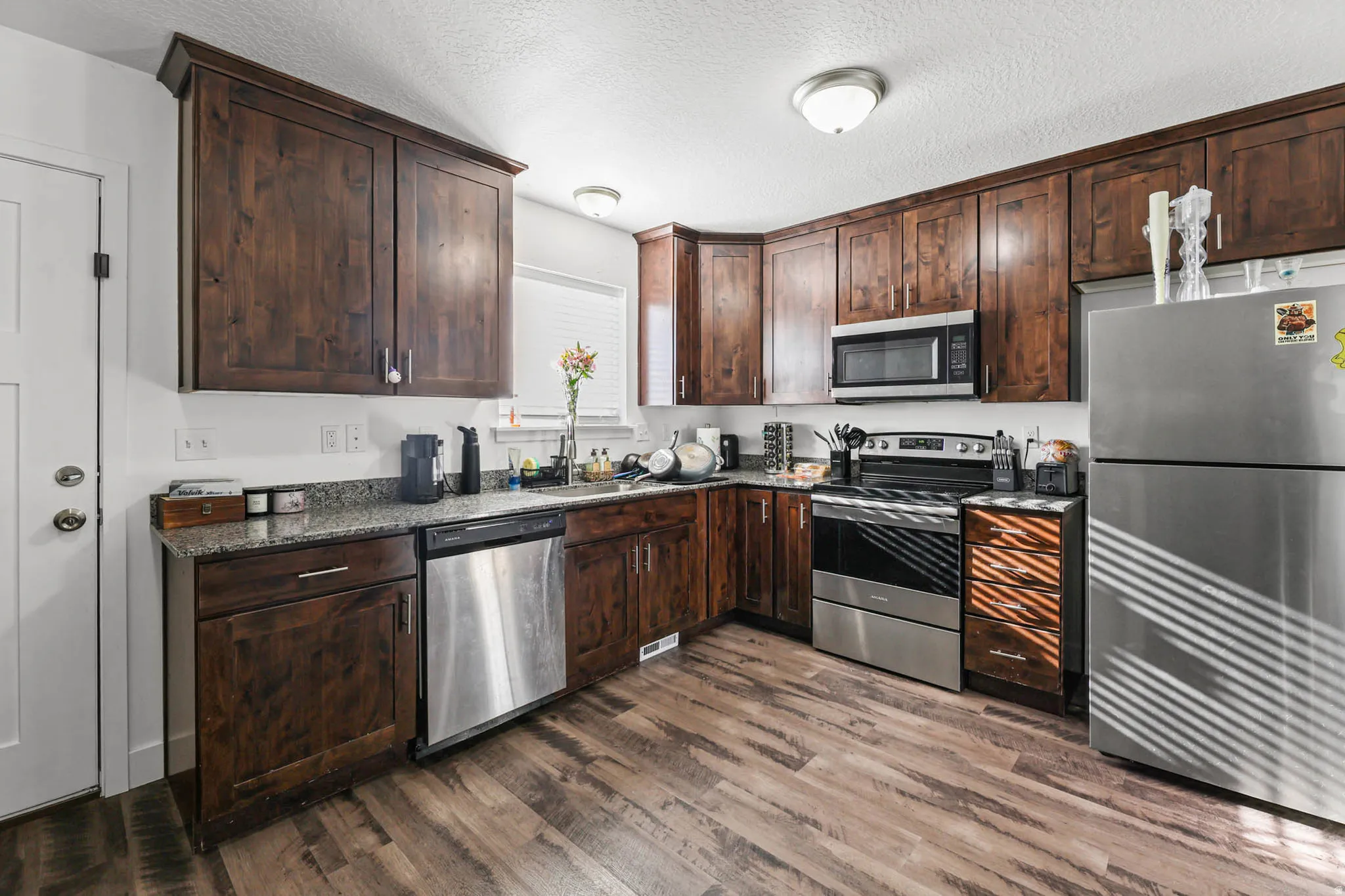 Kitchen with dark wood finish cabinets, stainless steel appliances, dark wood-style flooring, a textured ceiling, and dark stone countertops