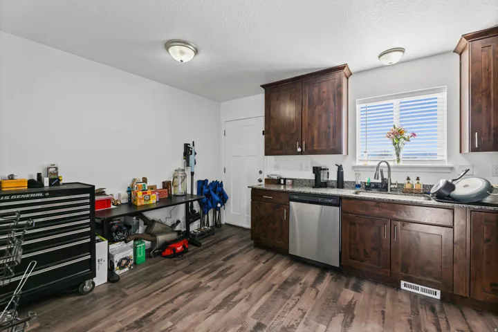 Kitchen featuring dark wood finish cabinets, stainless steel dishwasher, dark wood-style flooring, a textured ceiling, and light stone counters