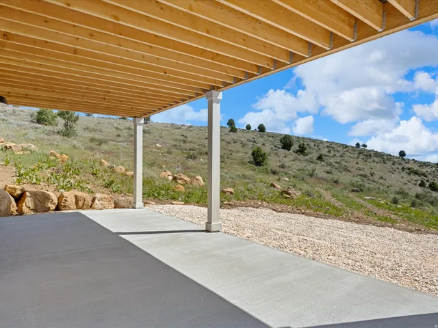 Covered concrete patio with two support columns, overlooking a sloped natural landscape with scattered trees and rock formations