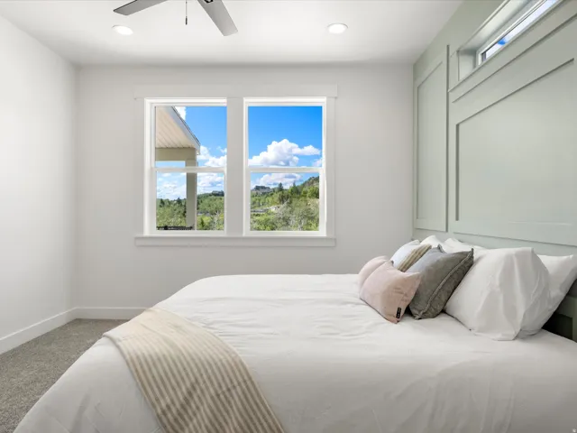 Bedroom featuring light-toned carpeting, a window wall with white trim, and a contemporary ceiling fan