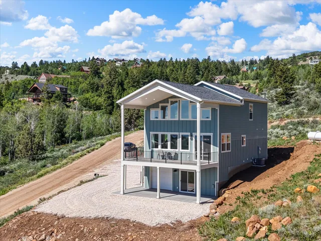 Modern two-story residence featuring a covered balcony, an abundance of windows, a lower-level patio, and a gravel driveway