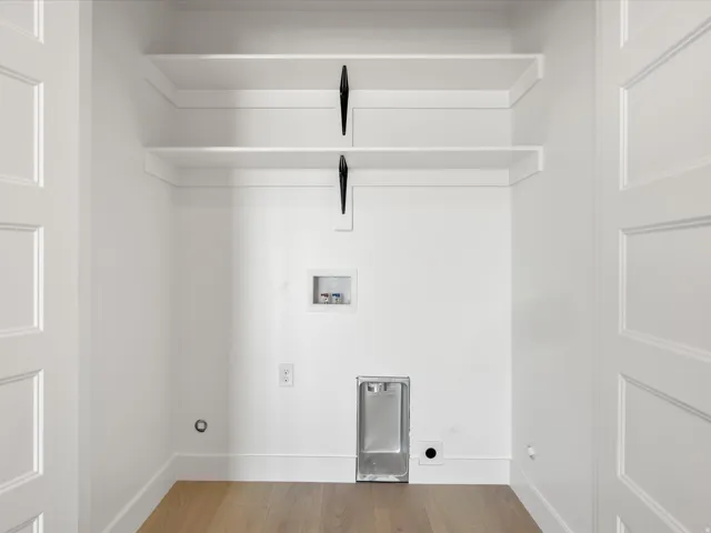 Dedicated laundry space featuring two built-in shelves, wood-finish flooring, and crisp white trim
