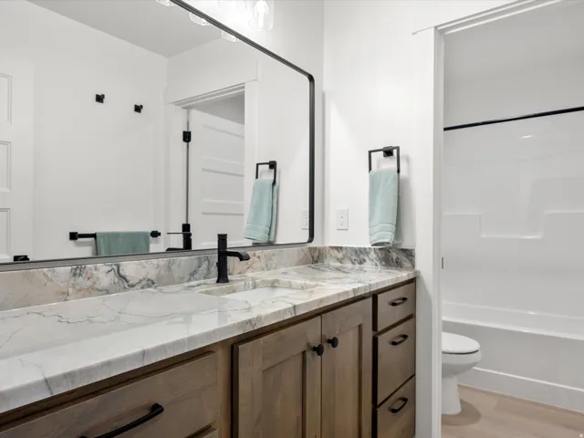 Bathroom vanity featuring a single sink with a matte black faucet, stone countertop with natural veining, and wood-finish cabinetry