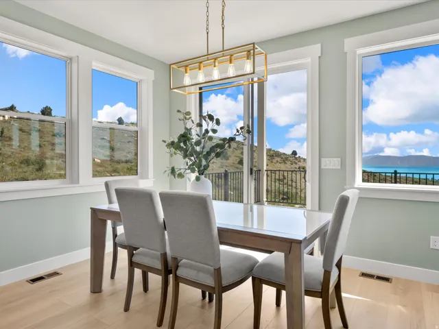 Dining area featuring light wood-finish flooring, a contemporary linear chandelier, and a sliding glass door leading to a balcony with a black metal railing