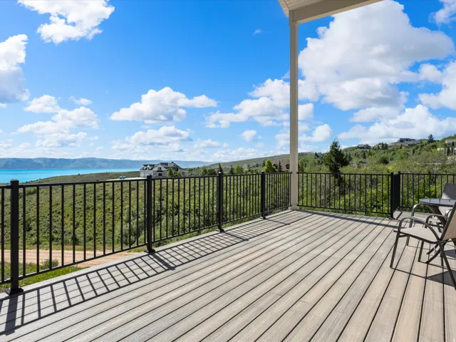 Spacious outdoor deck featuring composite decking, black metal railings, a partial overhead patio cover, and expansive water scenery with distant mountains