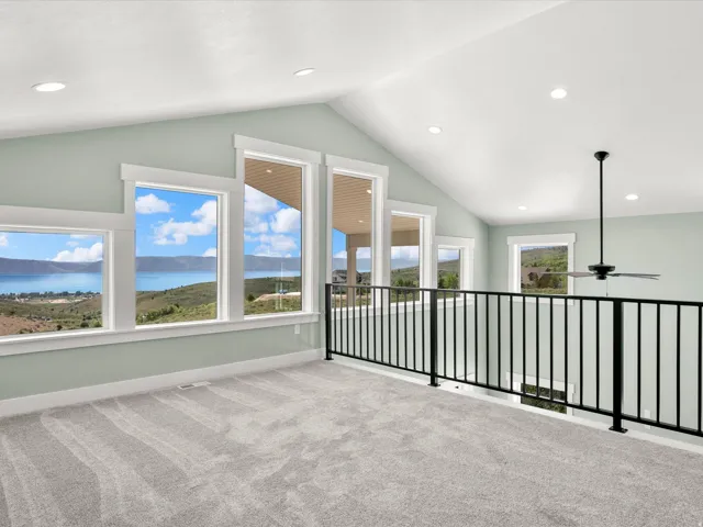 Spacious upper-level room featuring expansive windows, vaulted ceilings, recessed lighting, and soft grey carpeting