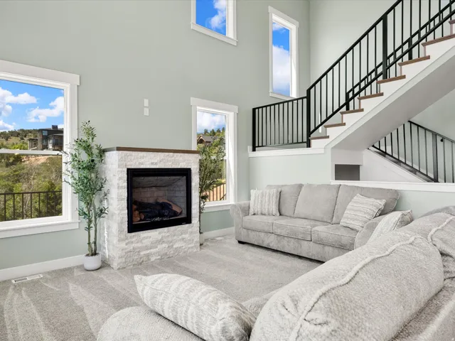 Two-story living area featuring a stacked stone fireplace with a dark wood mantel, multiple windows, and a staircase with open risers and black metal railings