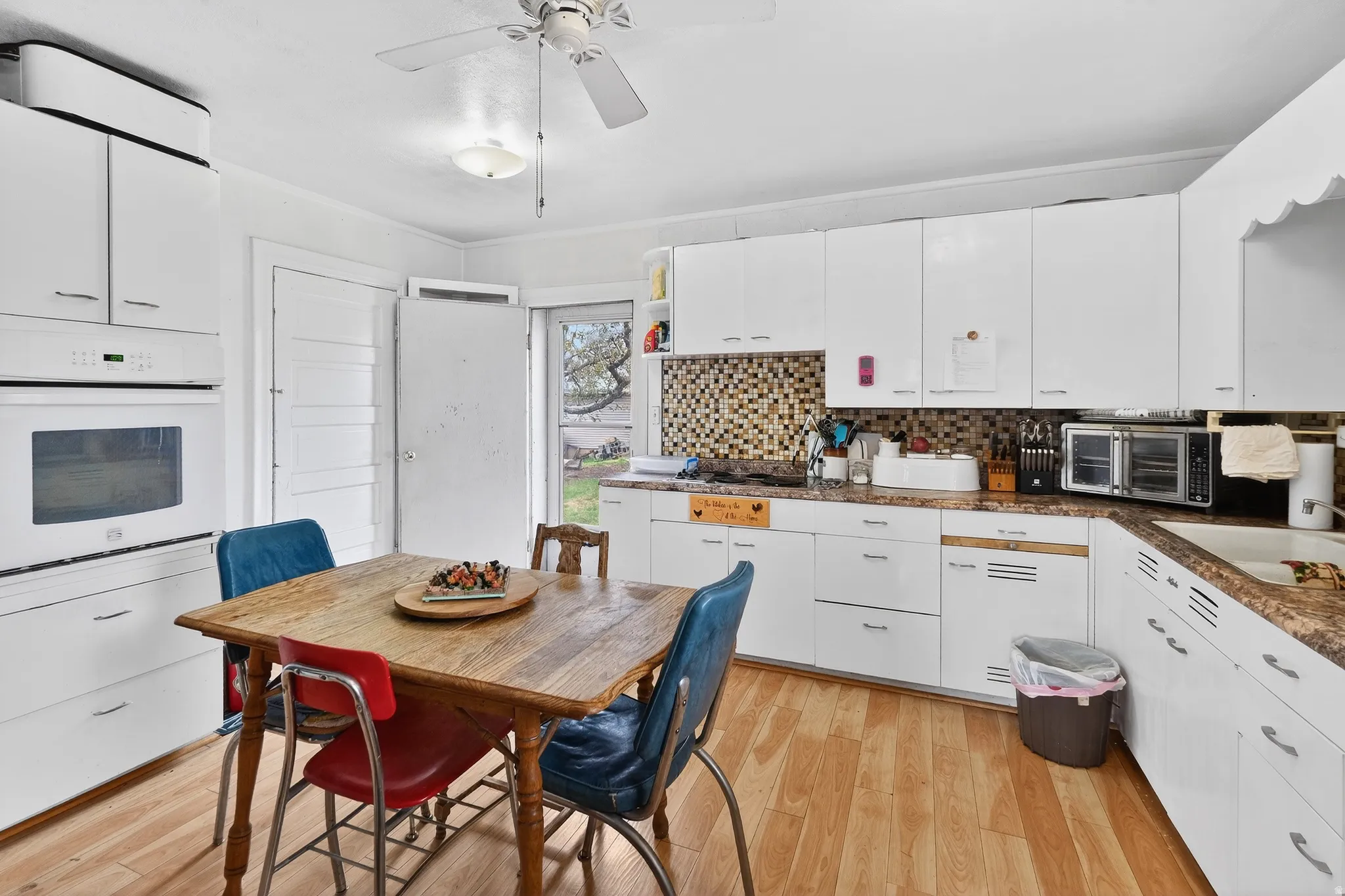 Kitchen featuring dark countertops, white oven, light wood-style flooring, ceiling fan, and white cabinetry