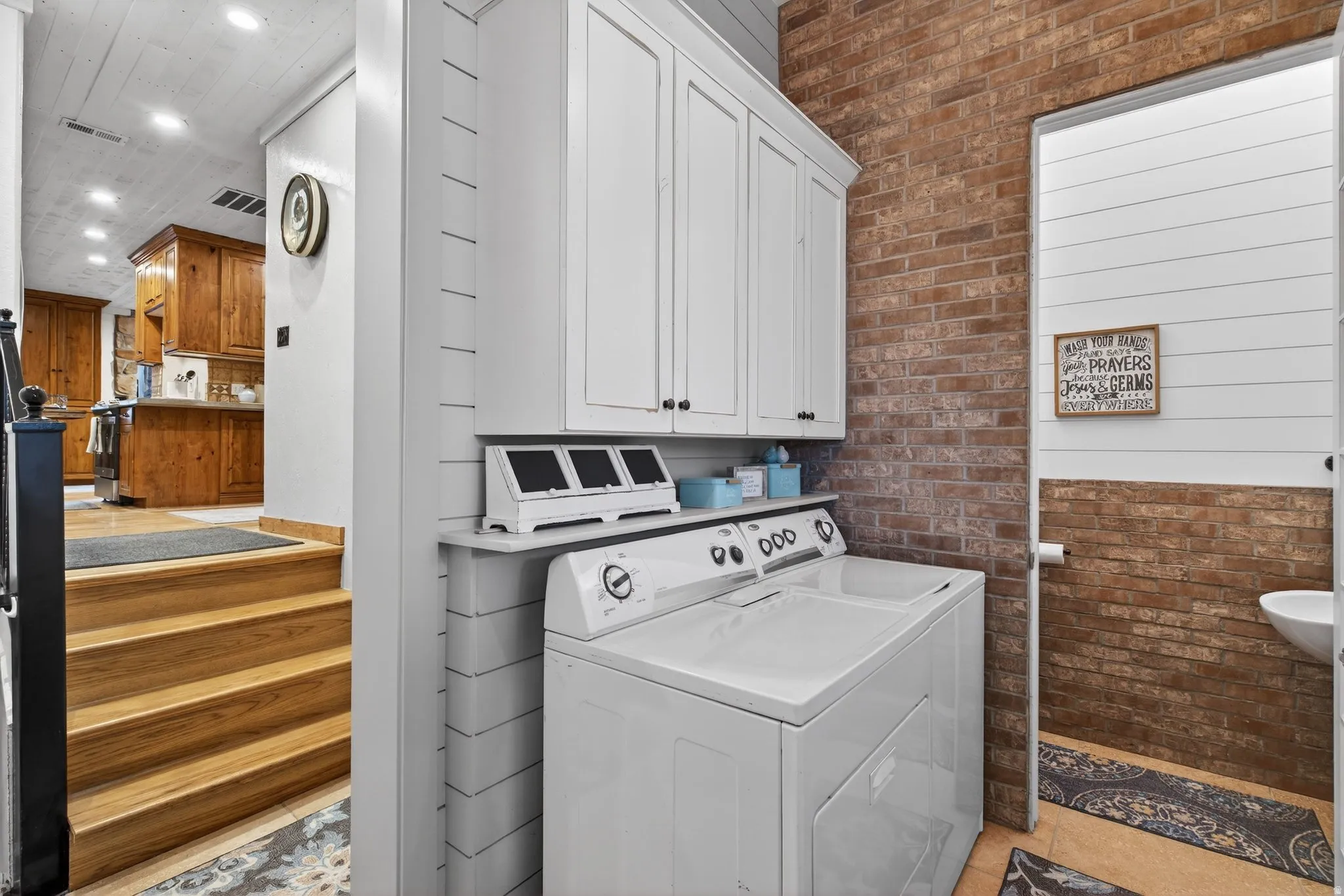 Laundry area with brick wall, washing machine and clothes dryer, cabinet space, and recessed lighting