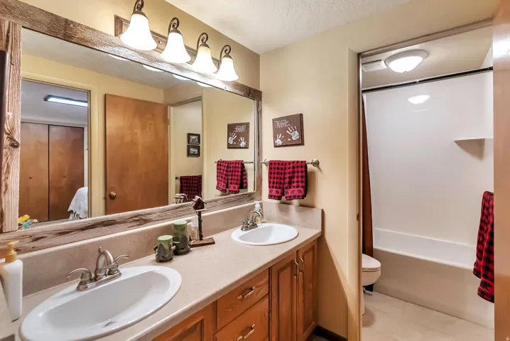 Bathroom featuring double vanity, a textured ceiling, connected bathroom, light tile patterned floors, and shower / bath combination