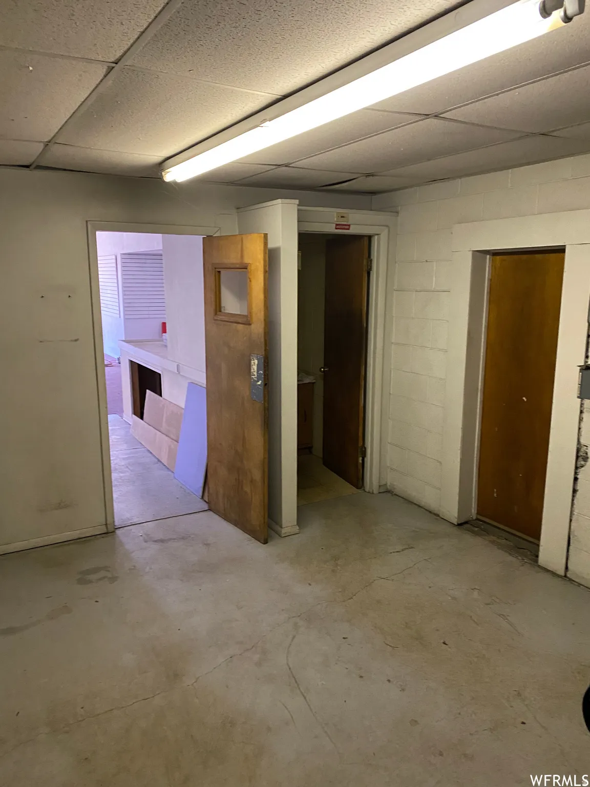 Unfurnished room featuring concrete block wall, a paneled ceiling, and concrete flooring