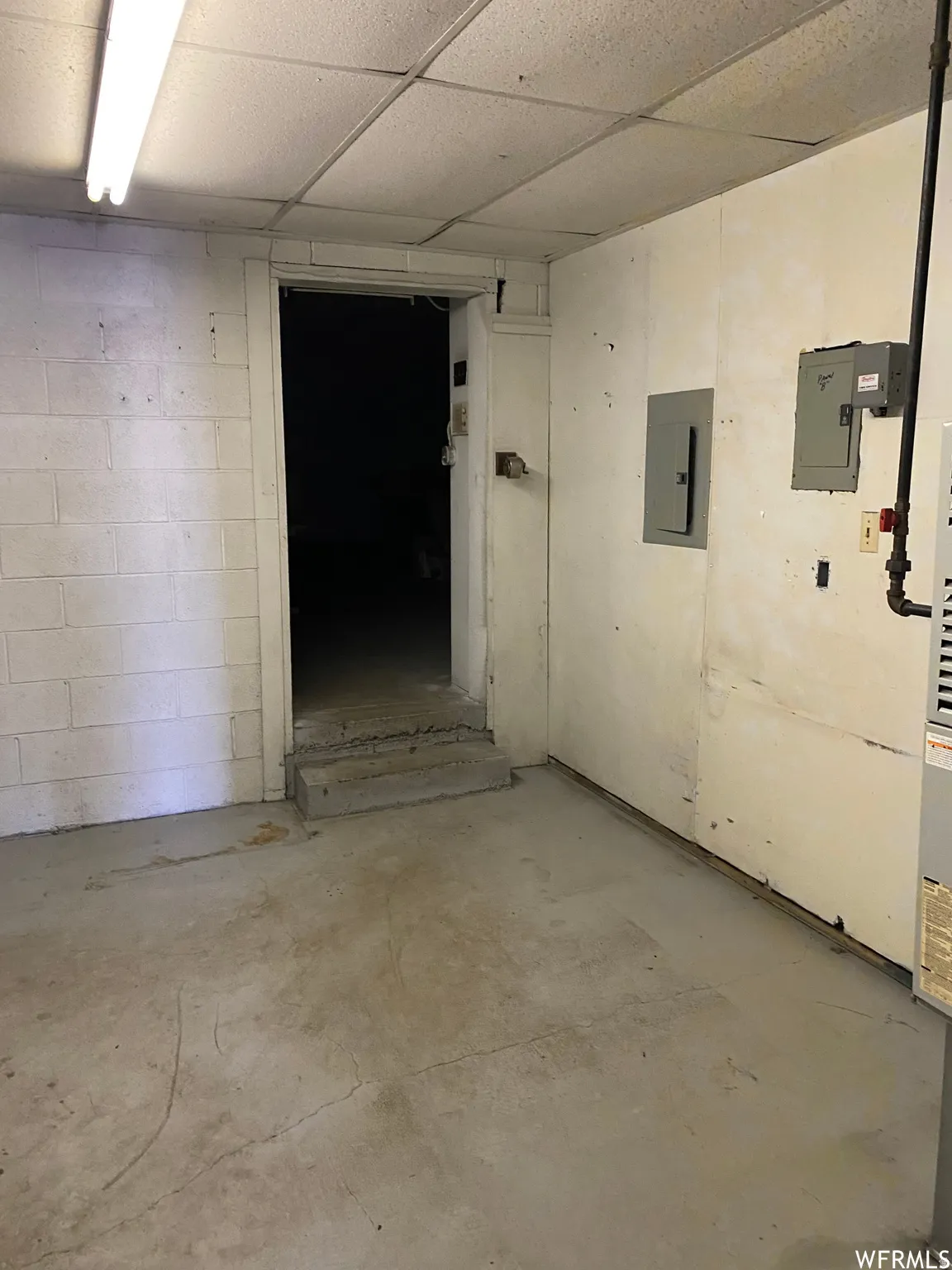 Basement featuring a drop ceiling, electric panel, and concrete block wall