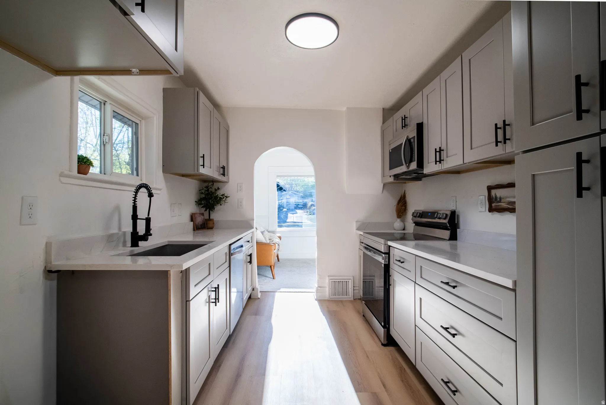 Kitchen featuring stainless steel appliances, arched walkways, light stone counters, gray cabinets, and light wood-style floors