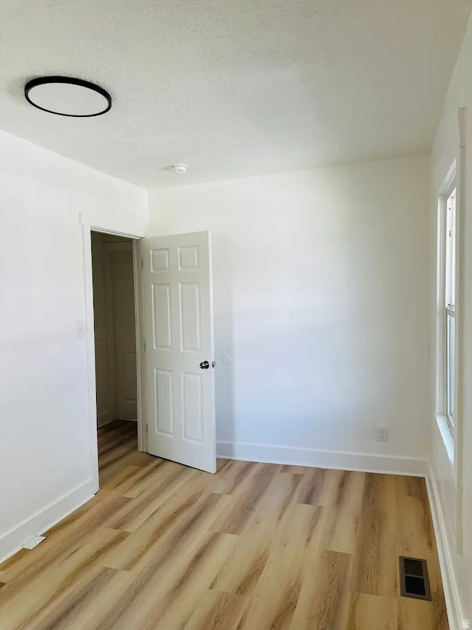 Empty room with a textured ceiling and light wood-type flooring