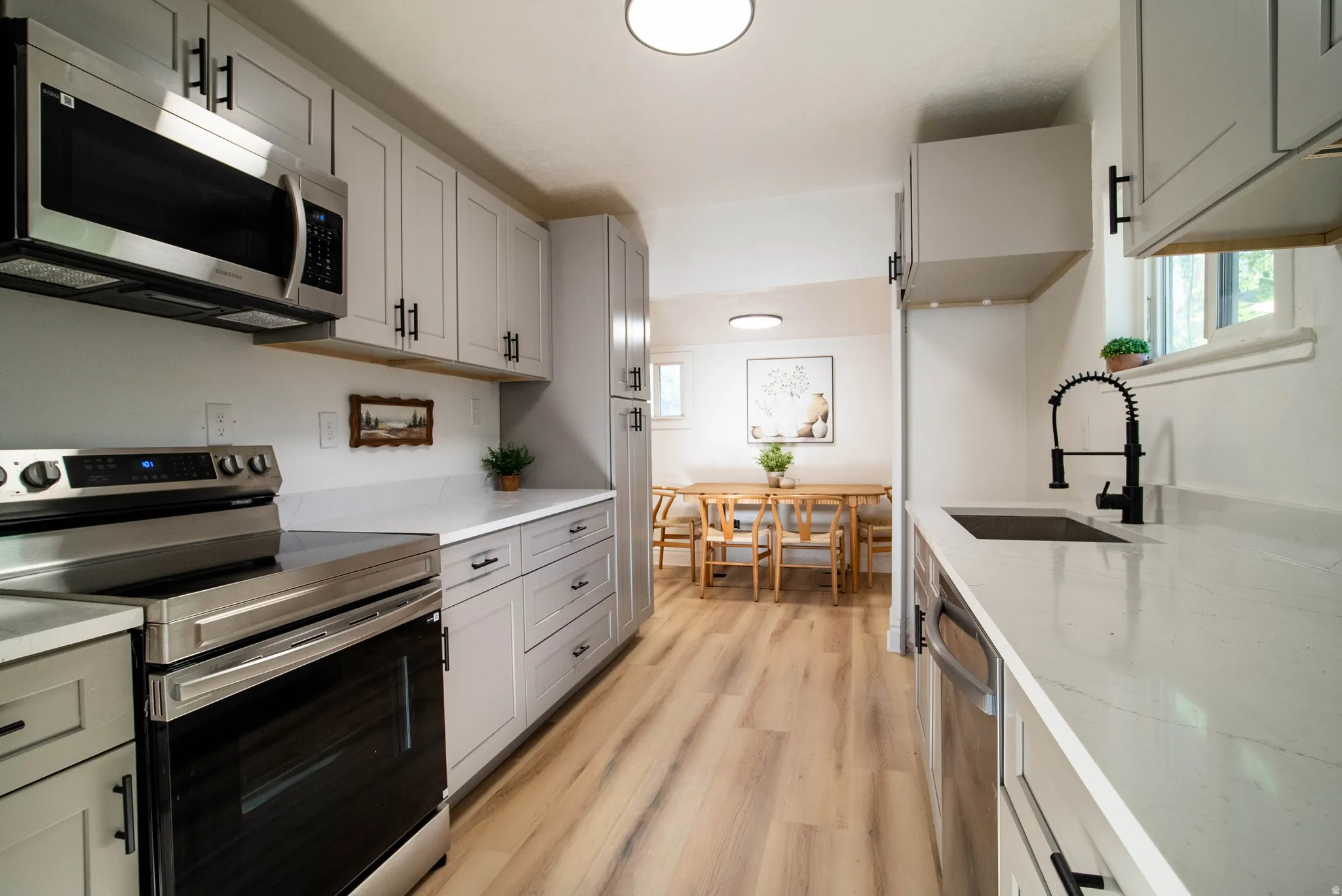 Kitchen with stainless steel appliances, gray cabinetry, light wood finished floors, and light stone countertops