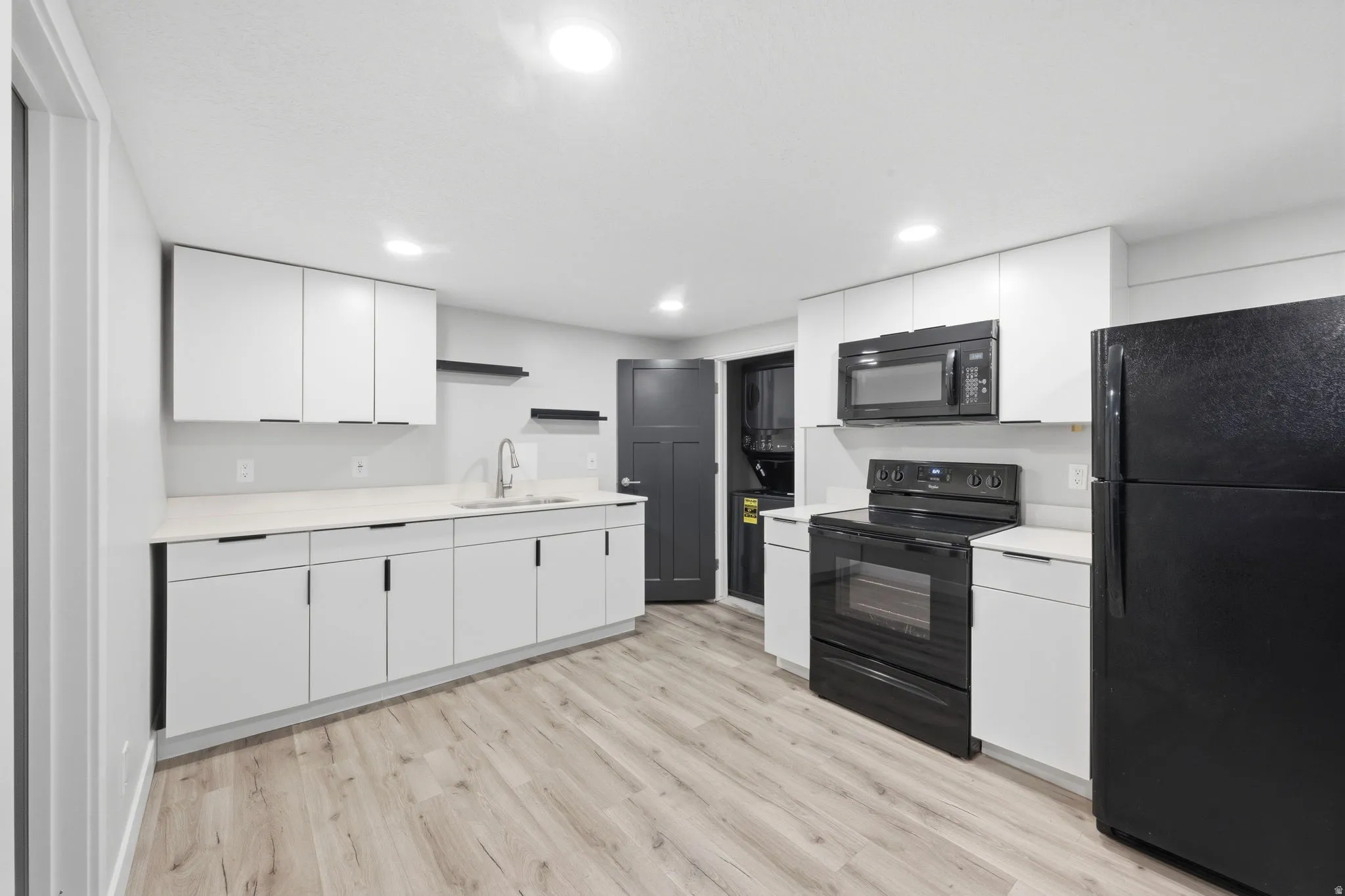 Kitchen featuring black appliances, light countertops, white cabinetry, light wood-style flooring, and recessed lighting