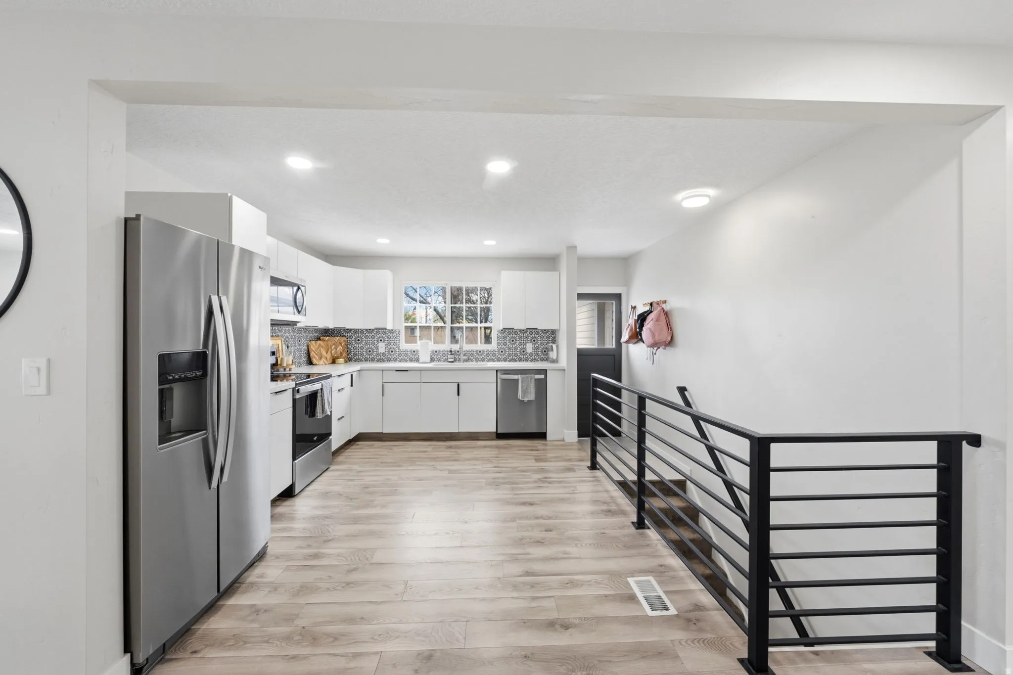Kitchen featuring stainless steel appliances, white cabinetry, light countertops, light wood-style flooring, and recessed lighting