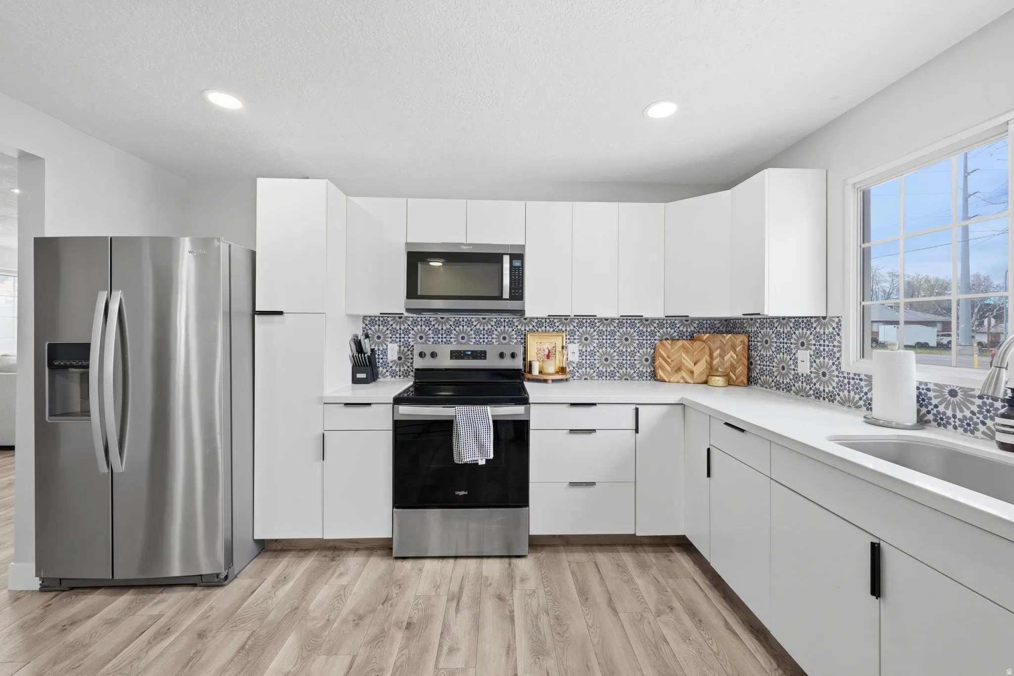 Kitchen with stainless steel appliances, white cabinetry, light wood-type flooring, recessed lighting, and backsplash