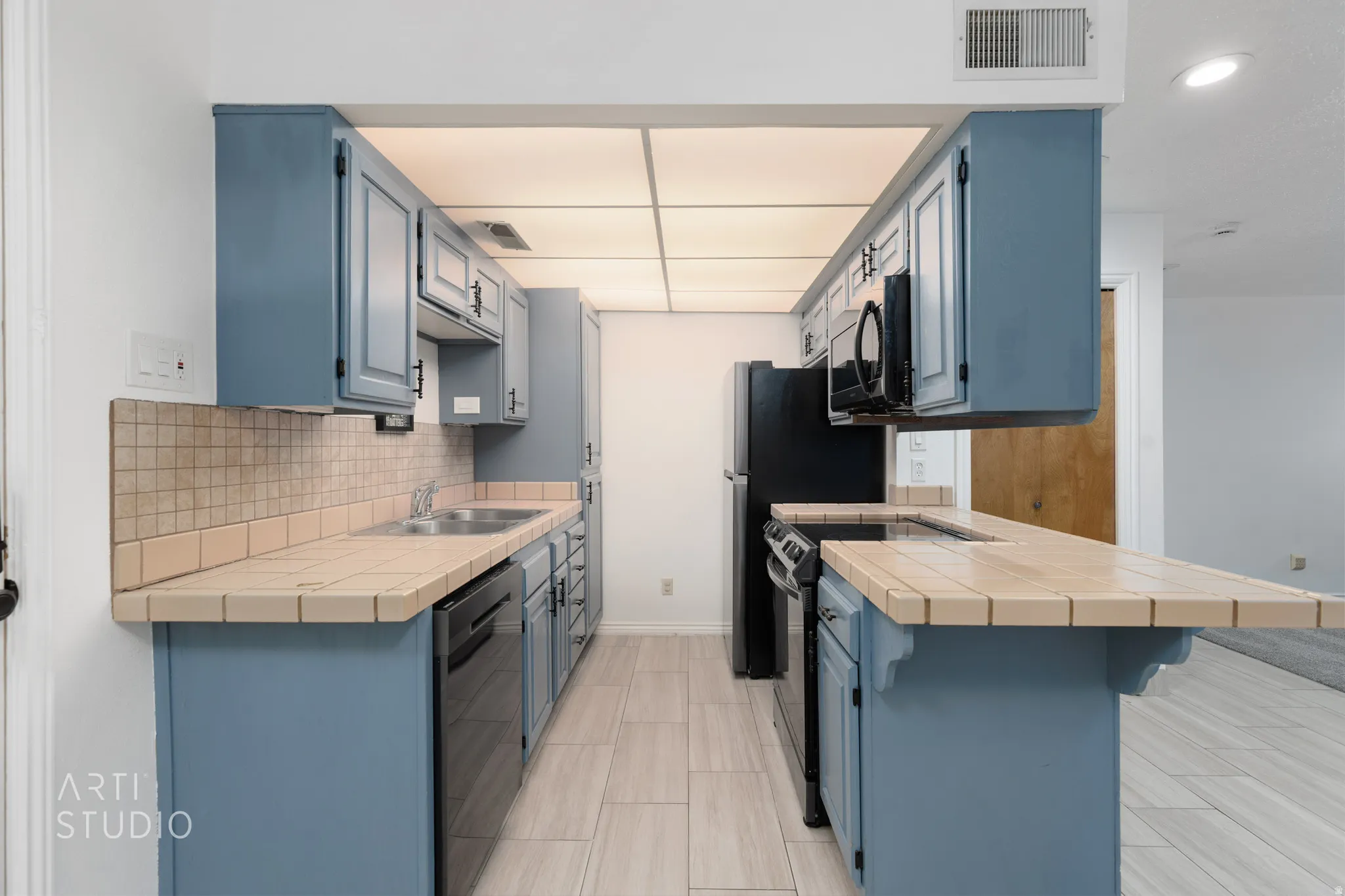 Kitchen featuring tile counters, a peninsula, blue cabinetry, a breakfast bar, and dishwasher