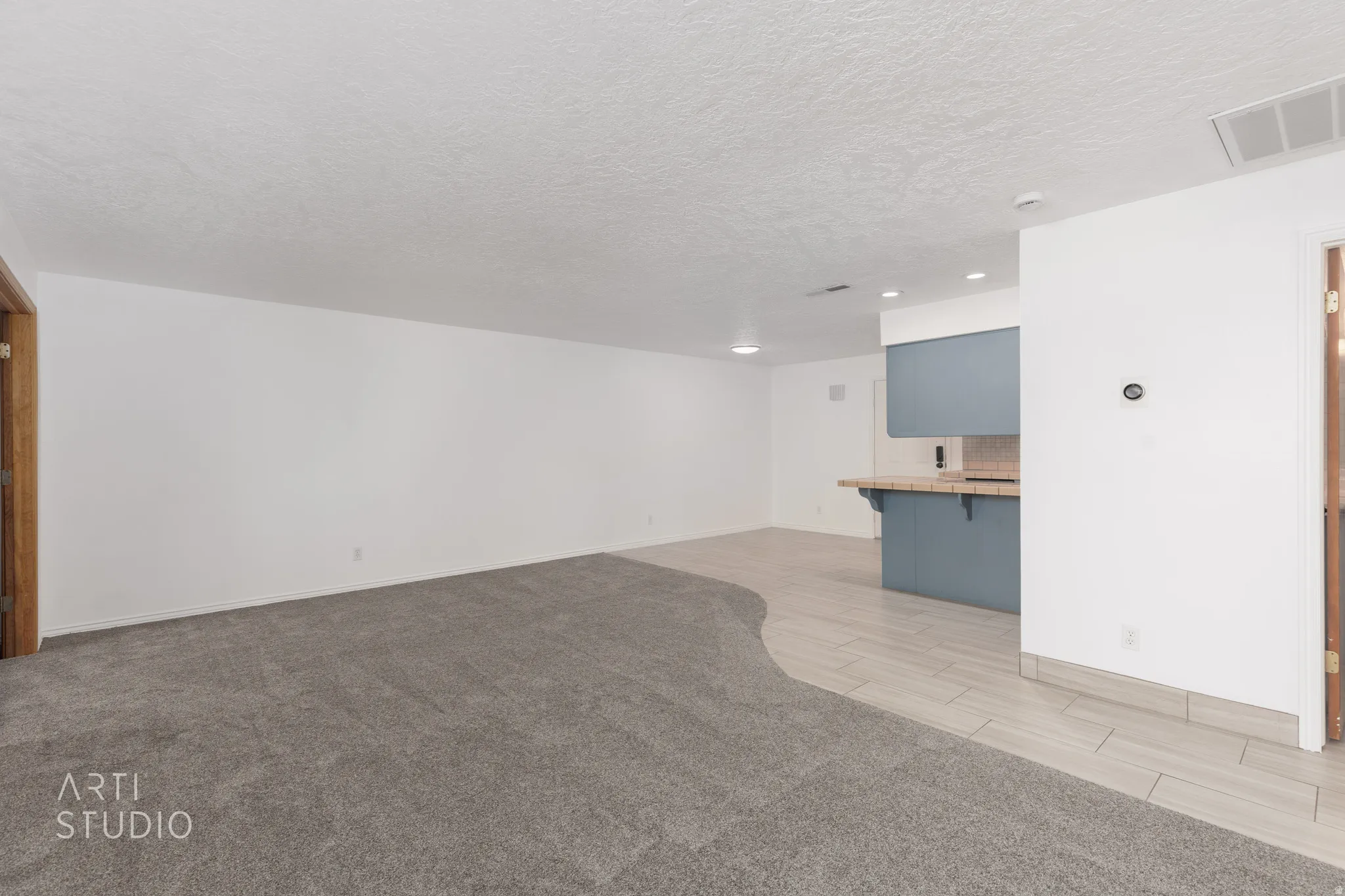 Unfurnished living room featuring a textured ceiling, light colored carpet, and wood finish floors