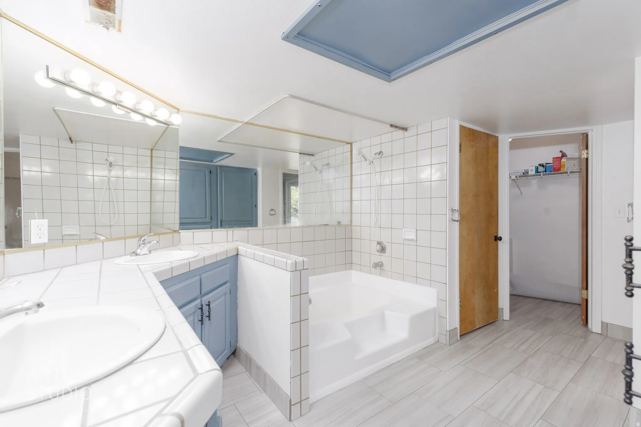 Full bathroom featuring double vanity, a walk in closet, a shower, a garden tub, and tile walls