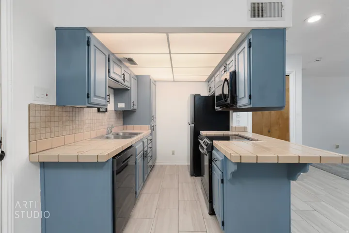 Kitchen featuring tile counters, a peninsula, blue cabinetry, a breakfast bar, and dishwasher