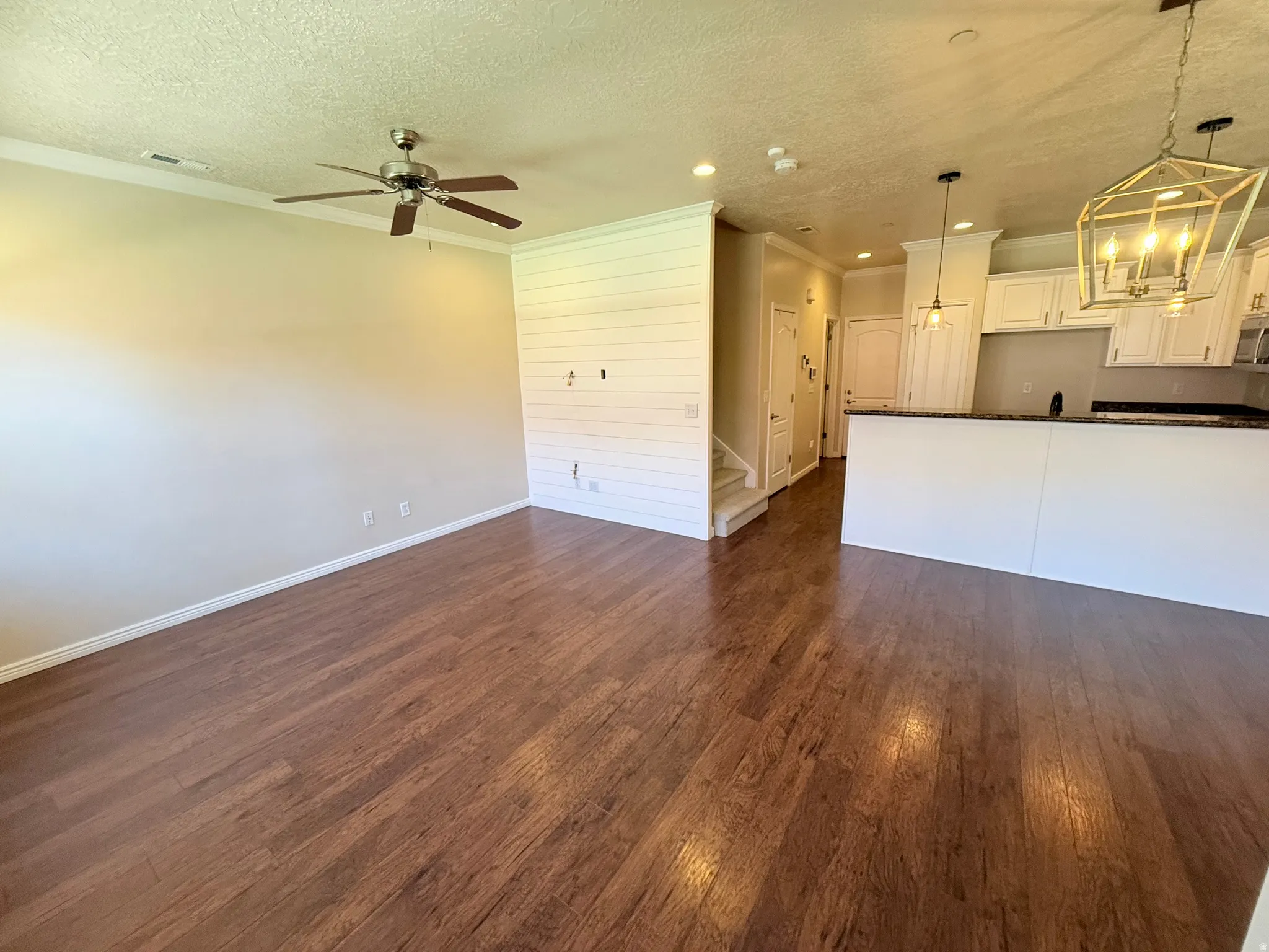 Unfurnished living room with ornamental molding, a textured ceiling, dark wood-style floors, a ceiling fan, and hanging lights