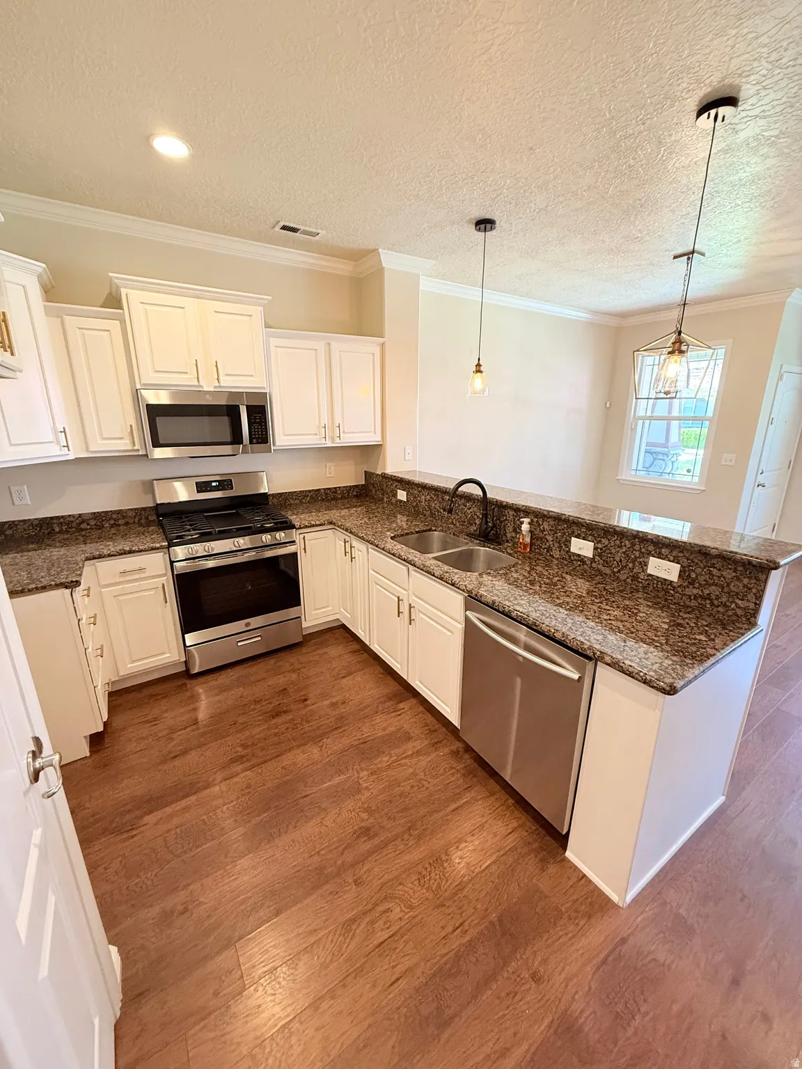 Kitchen with stainless steel appliances, dark stone counters, white cabinetry, ornamental molding, and a textured ceiling