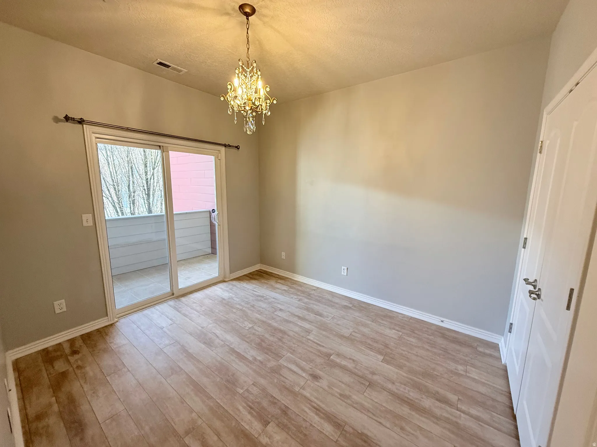Spare room featuring light wood-style floors, hanging lights, and a textured ceiling