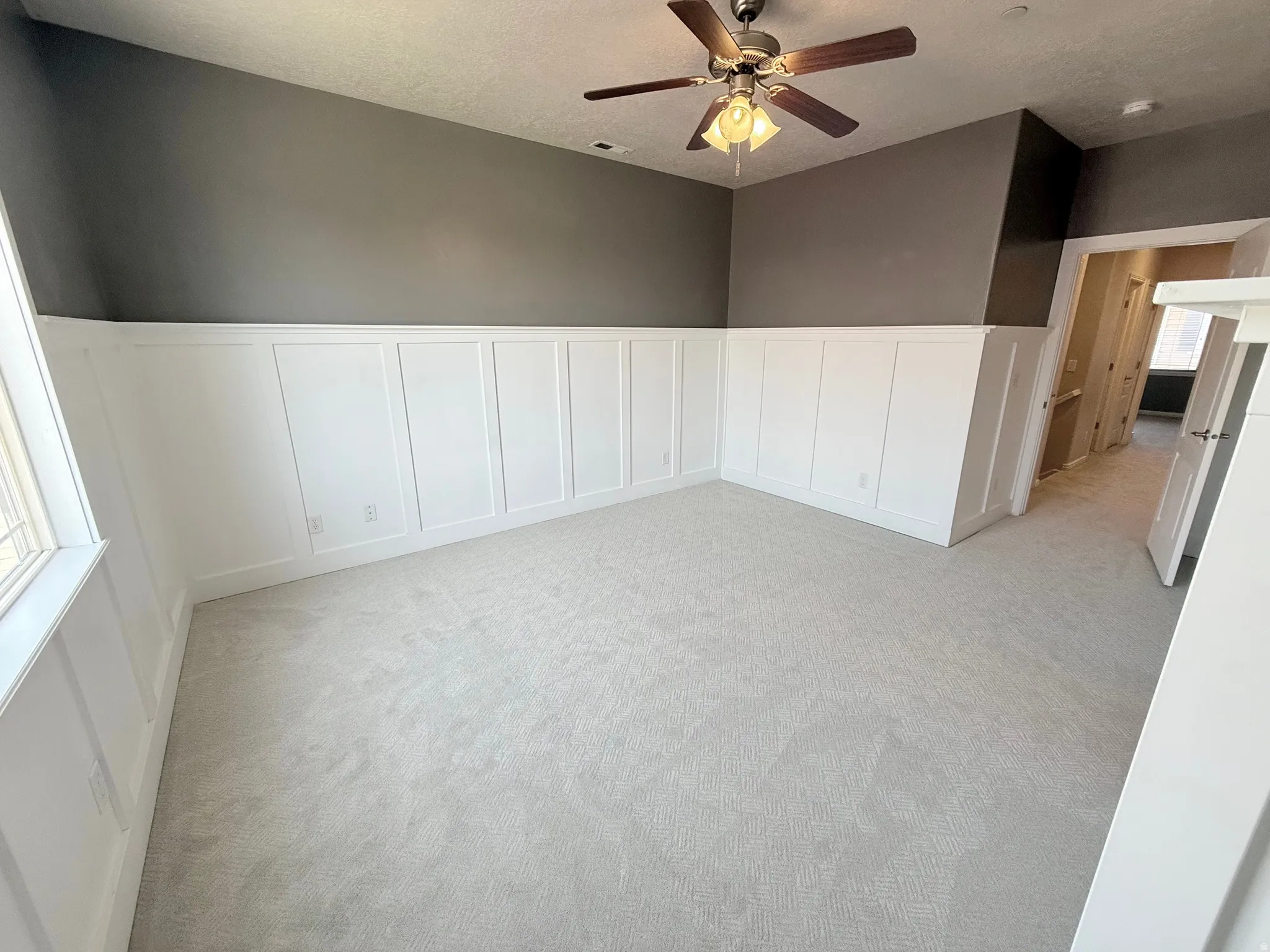 Spare room featuring a wainscoted wall, a decorative wall, light carpet, a ceiling fan, and a textured ceiling