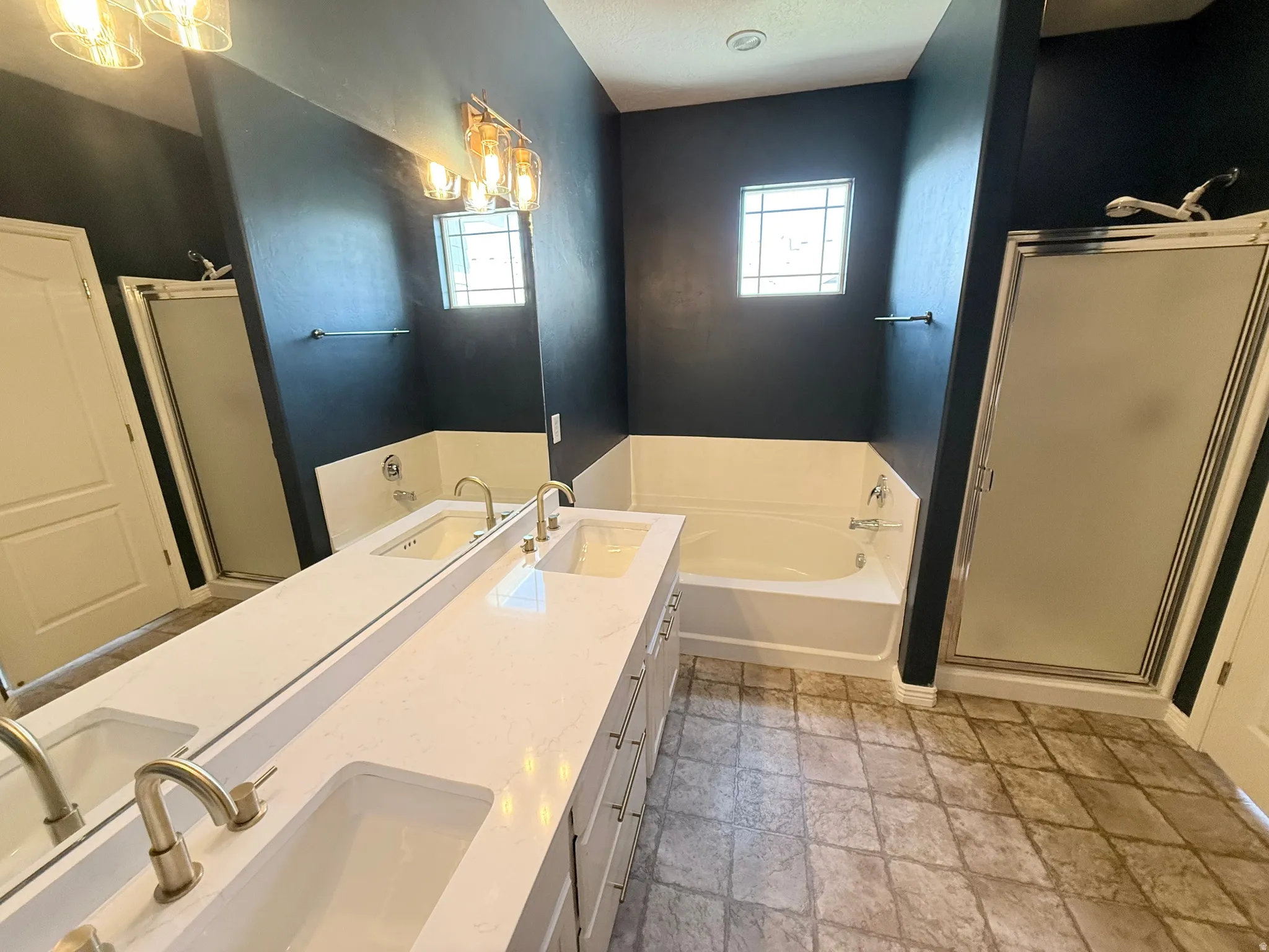 Bathroom featuring a stall shower, double vanity, a bath, and light stone finish flooring