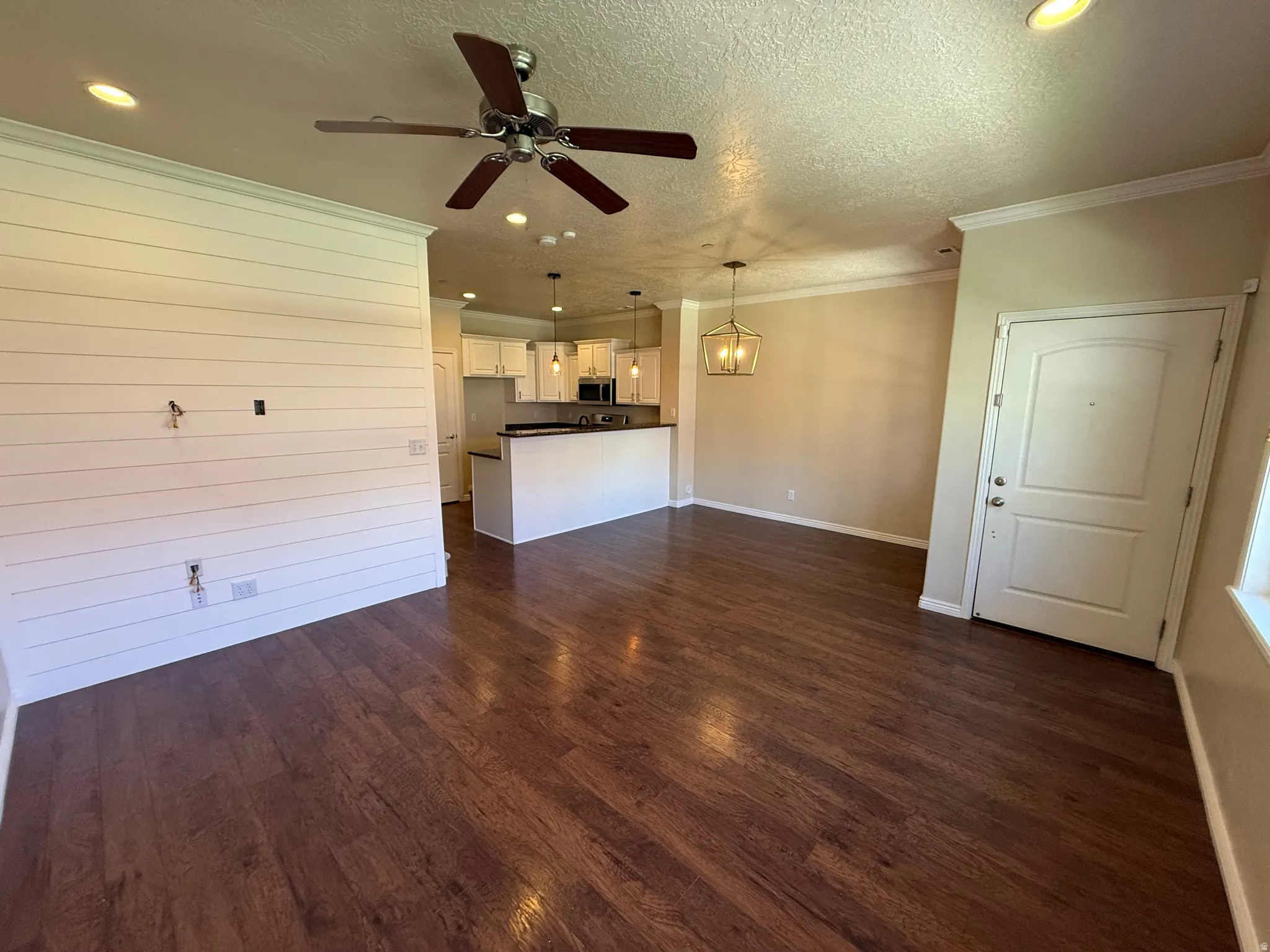 Unfurnished living room with a textured ceiling, dark wood-style flooring, ornamental molding, a ceiling fan, and suspended lighting