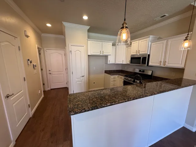 Kitchen featuring a peninsula, white cabinets, stainless steel appliances, dark stone counters, and decorative light fixtures