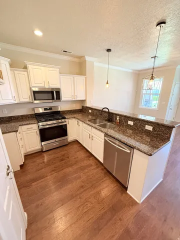 Kitchen with stainless steel appliances, dark stone counters, white cabinetry, ornamental molding, and a textured ceiling