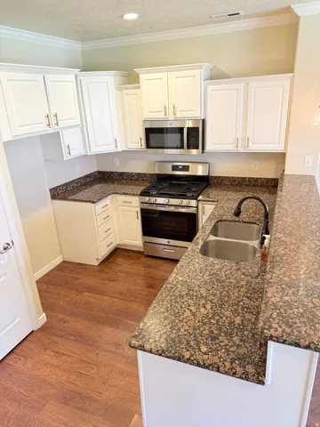 Kitchen featuring stainless steel appliances, dark stone countertops, white cabinetry, a peninsula, and a textured ceiling