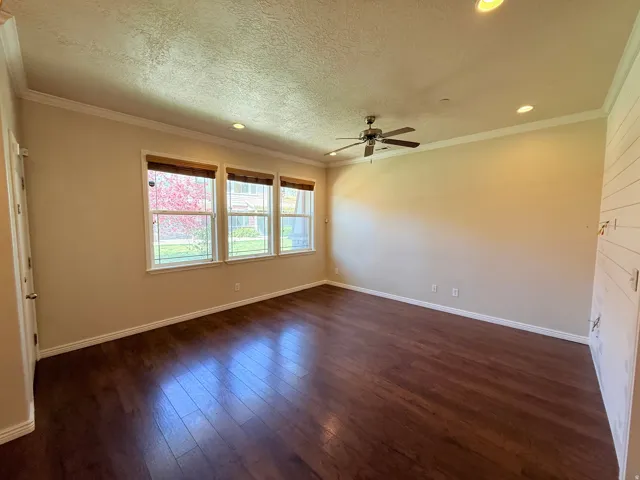Empty room featuring dark wood-style floors, a textured ceiling, recessed lighting, a ceiling fan, and crown molding