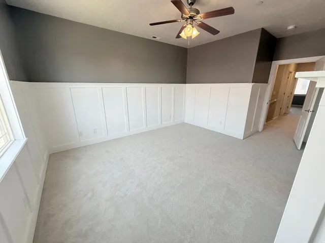Spare room featuring a wainscoted wall, a decorative wall, light carpet, a ceiling fan, and a textured ceiling