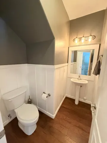 Half bath featuring dark wood-style floors, a wainscoted wall, and a decorative wall