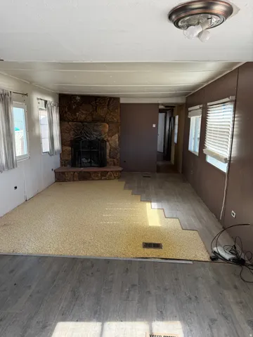 Living area featuring a stone-clad fireplace with hearth, partial wood-finish flooring, and multiple windows