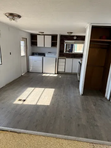 Open-concept area featuring wood-finish flooring, a full kitchen with white cabinetry and a brick-patterned backsplash, and a dedicated laundry area