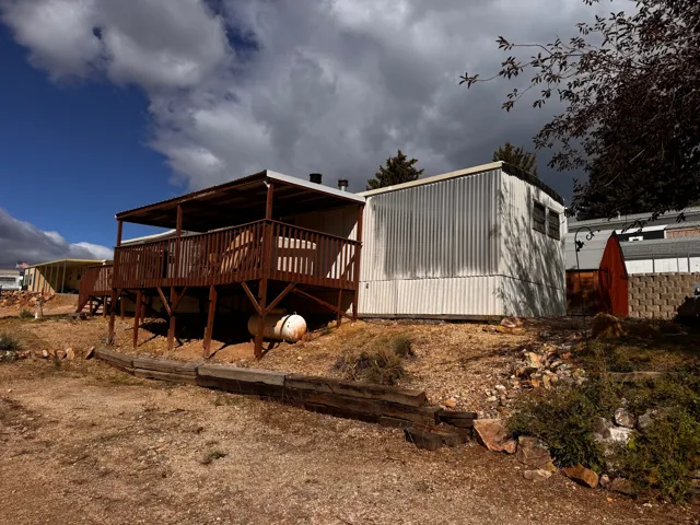 Exterior featuring a covered wood deck with railings, corrugated metal siding, and a sloped, natural terrain
