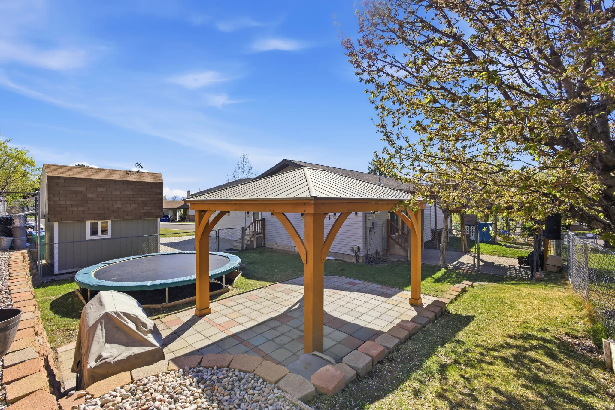 Fenced backyard featuring a gazebo, a trampoline, a patio, and a storage unit
