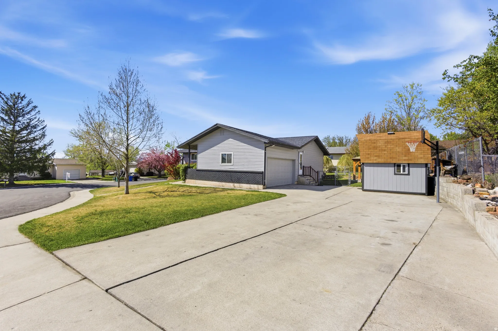 View of property exterior with concrete driveway, an outbuilding, a shingled roof, and an attached garage