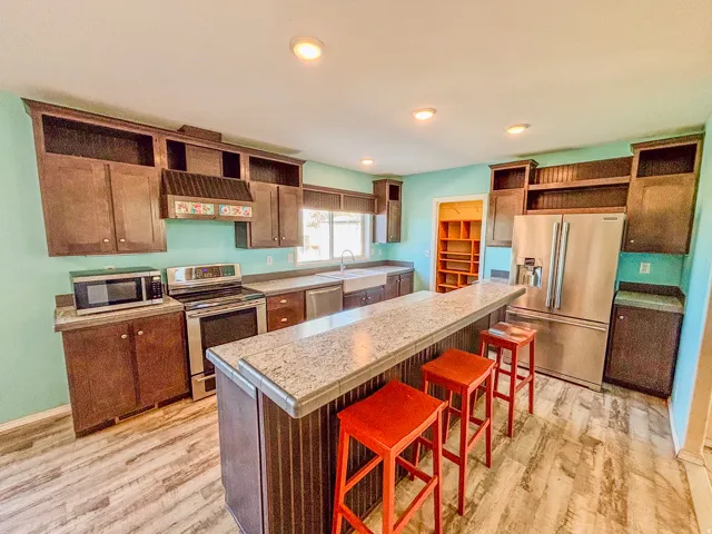 Kitchen with open shelves, stainless steel appliances, a kitchen island, a breakfast bar area, and light wood-style floors