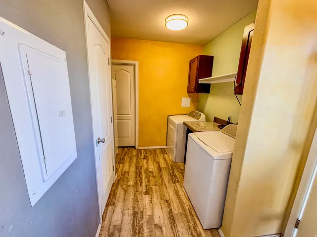 Laundry area with cabinet space, light wood finished floors, independent washer and dryer, and a textured ceiling