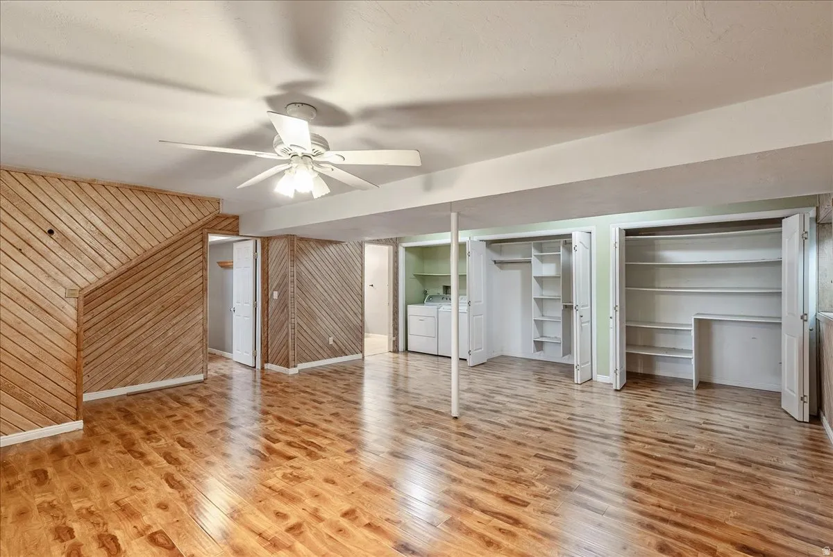 Unfurnished living room with ceiling fan, wooden walls, light wood-type flooring, and independent washer and dryer