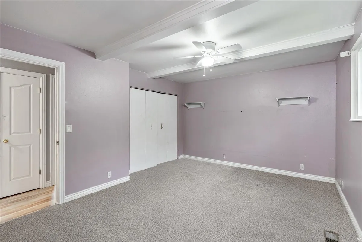 Unfurnished bedroom featuring light carpet, beam ceiling, a closet, and ceiling fan