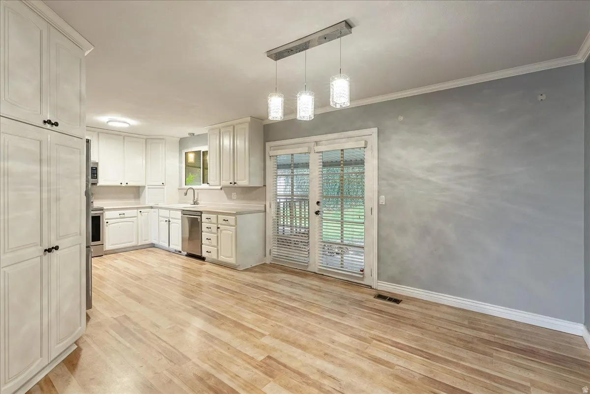 Kitchen with light countertops, light wood-style flooring, stainless steel appliances, hanging light fixtures, and white cabinets